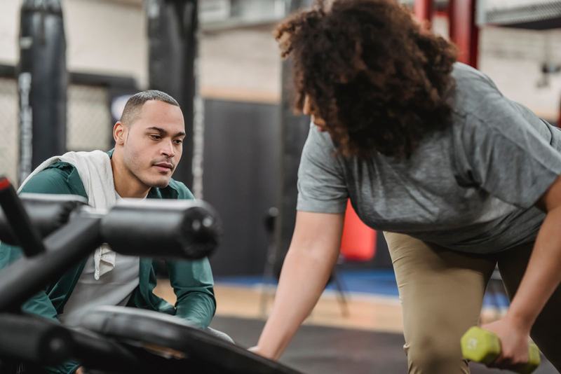 Professora orientando uma aluna que faz exercício com halteres