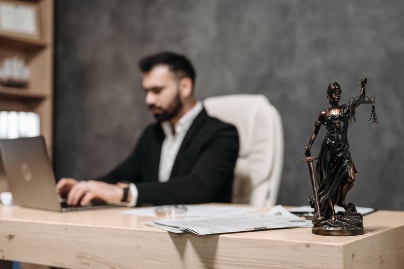 Advogado trabalhando no notebook em uma mesa, com uma estatueta da justiça em primeiro plano