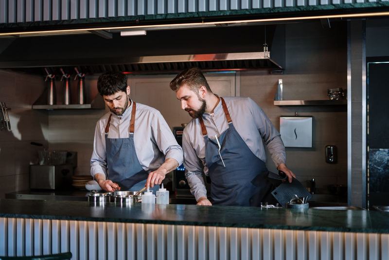 Dois cozinheiros de avental trabalhando lado a lado em uma cozinha aberta
