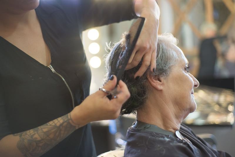 Cabeleireira cortando o cabelo grisalho de uma cliente diante do espelho